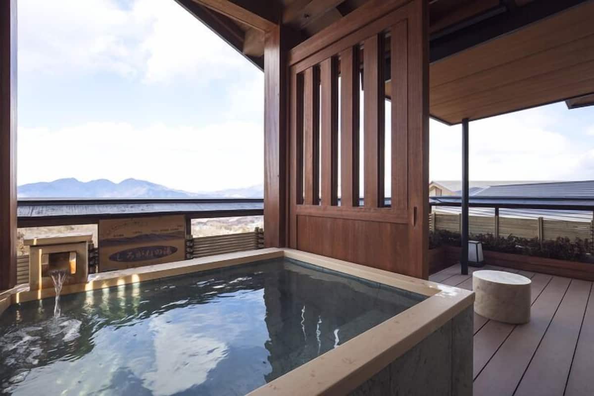 Un área de aguas termales con una terraza de madera, un banco de piedra y vistas a montañas.