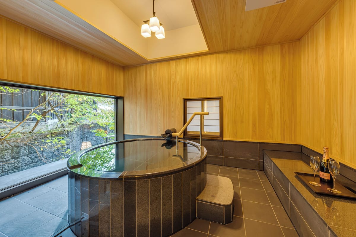 Un baño moderno con bañera de hidromasaje con mampara de vidrio, detalles de madera y vistas al exterior.