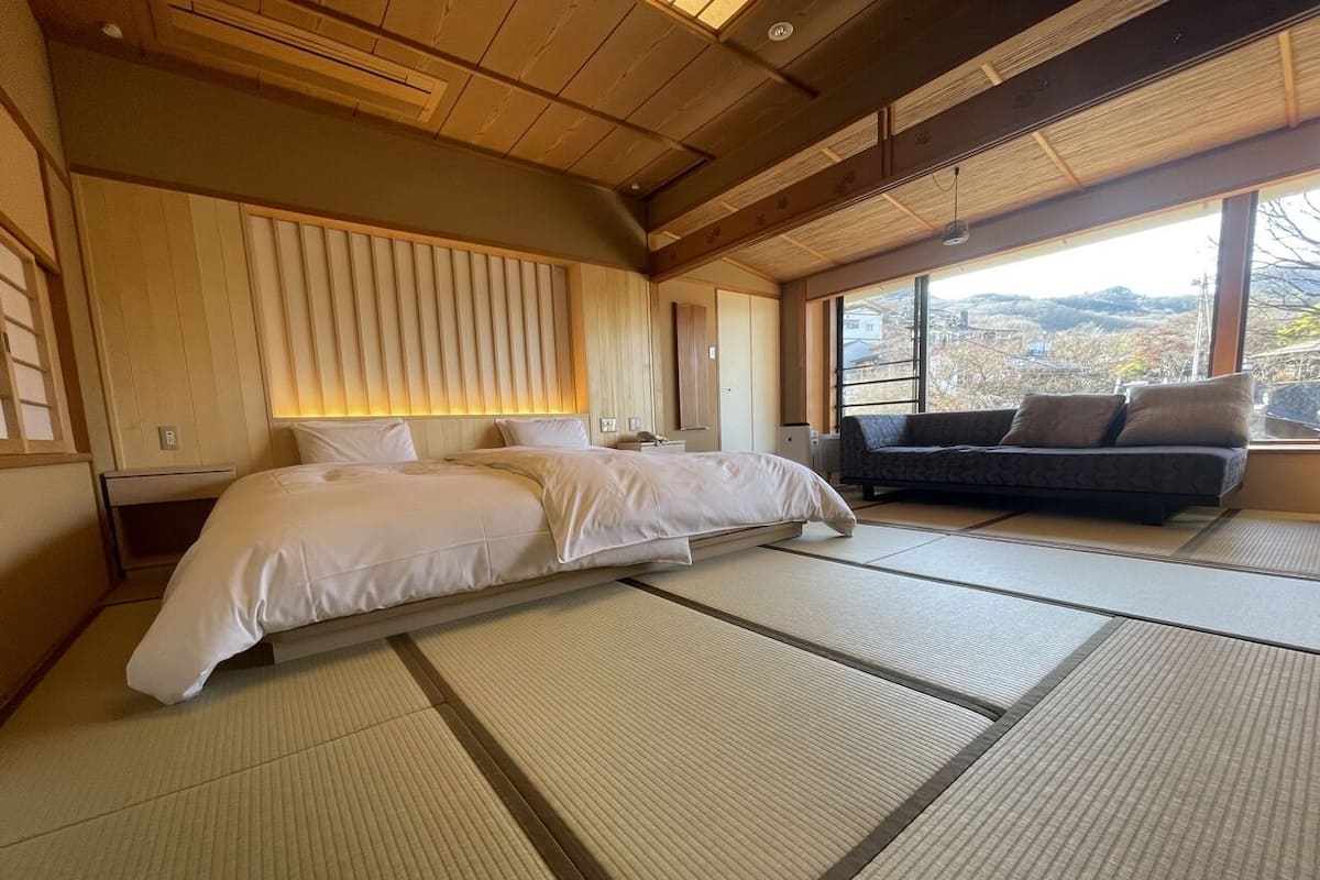 Una habitación japonesa tradicional con suelo de tatami, una cama, un sofá y vistas al exterior.