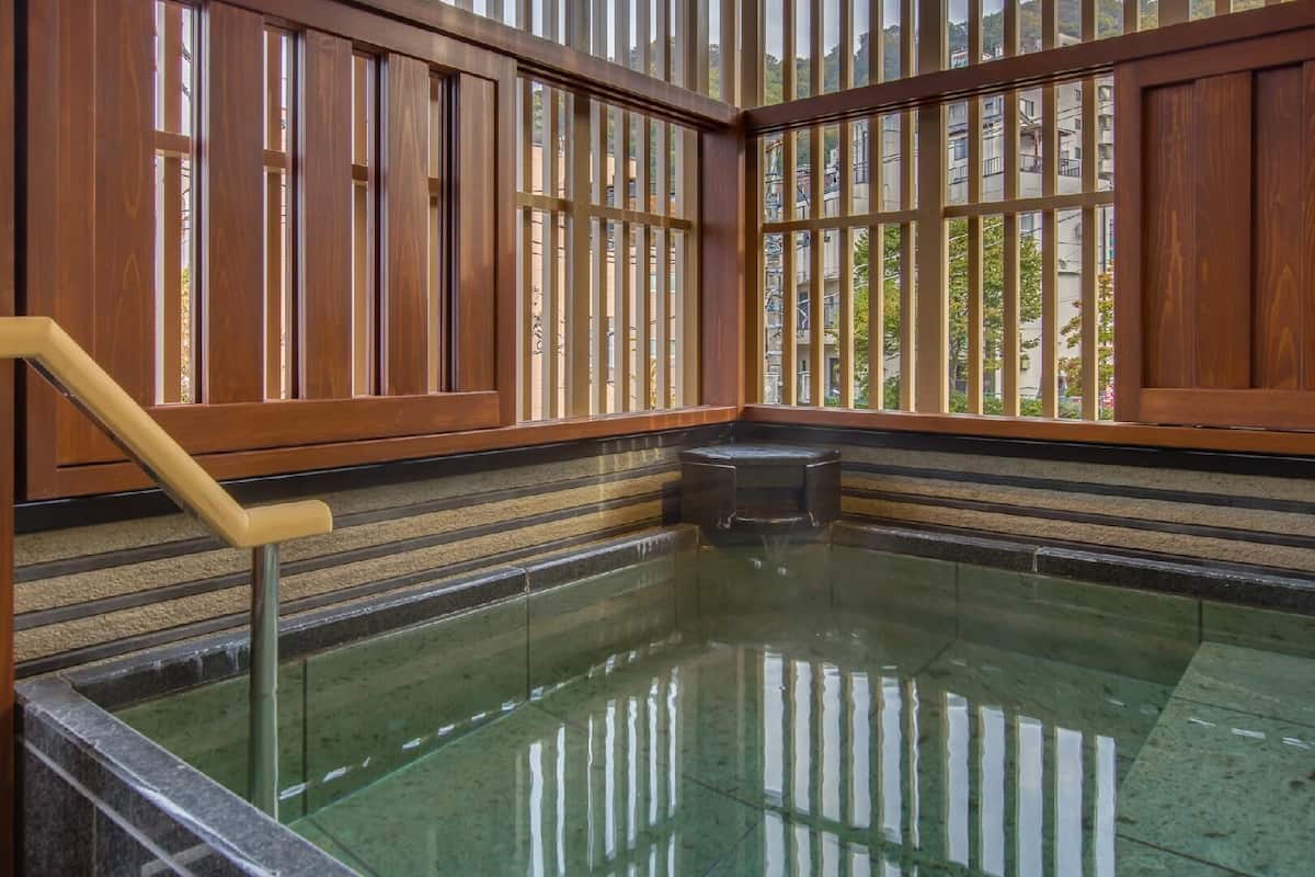 Un onsen japonés tradicional con puertas correderas de madera, un banco de piedra y una piscina de agua cristalina.