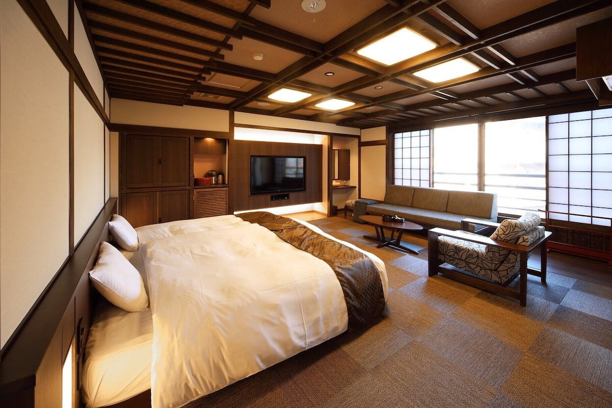 Una habitación de hotel con cama, sofá, televisor y un amplio ventanal.