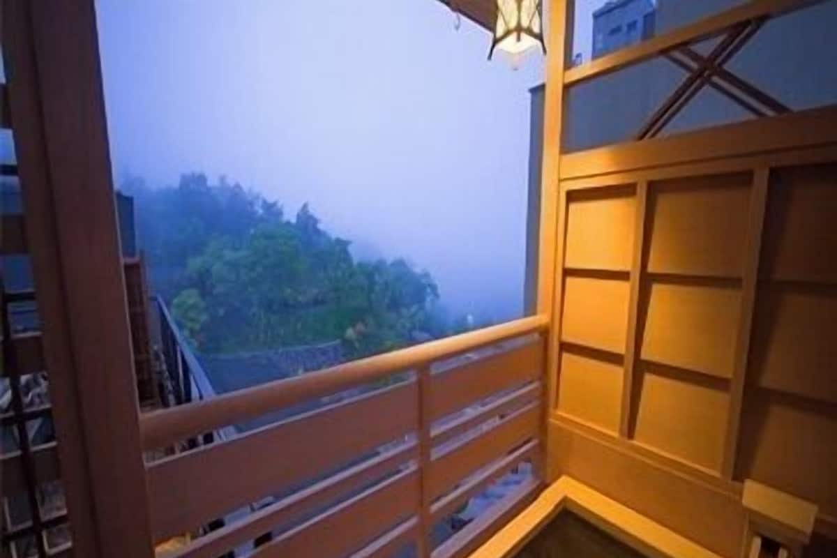 Una habitación con balcón de madera, vistas a follaje y una puerta corredera tradicional japonesa.