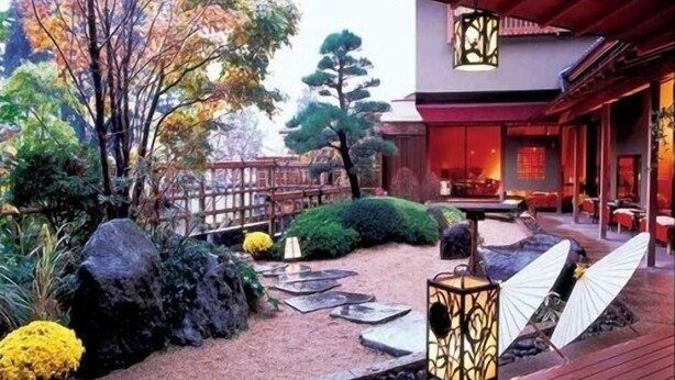 Un jardin de style japonais traditionnel, agrémenté d’une terrasse en bois, de lanternes et d’une variété de plantes et de rochers.