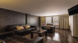 A modern living room with a dark leather sofa, a smaller armchair, and a coffee table. There is a window with curtains and a flat-screen TV mounted on the wall. - Suites Meson del Cid (Xalapa)