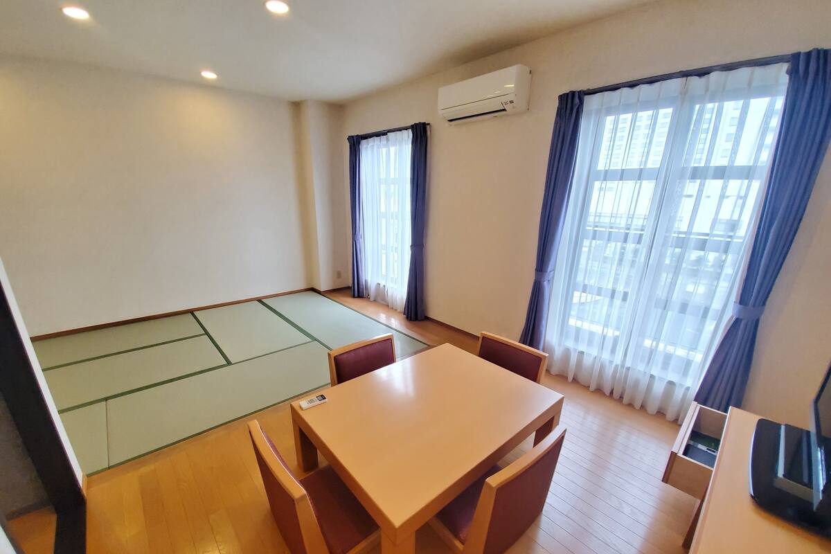 A room with tatami flooring, a wooden table with chairs, a TV, and an air conditioning unit.