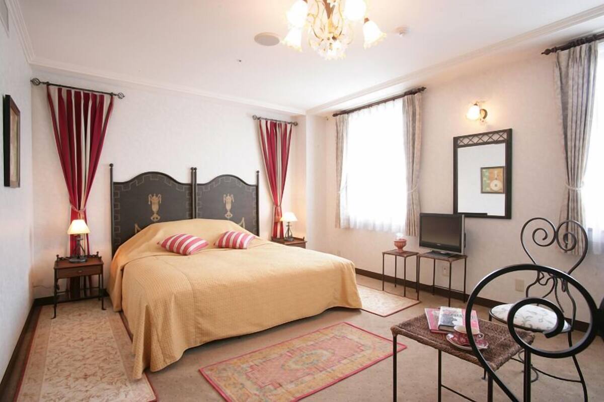A bedroom with a large bed, a television, a chandelier, and a mirror on the wall.