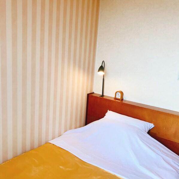 A hotel room with a striped wall, a wooden headboard, a bed with white sheets, a lamp, and a small clock on the headboard.