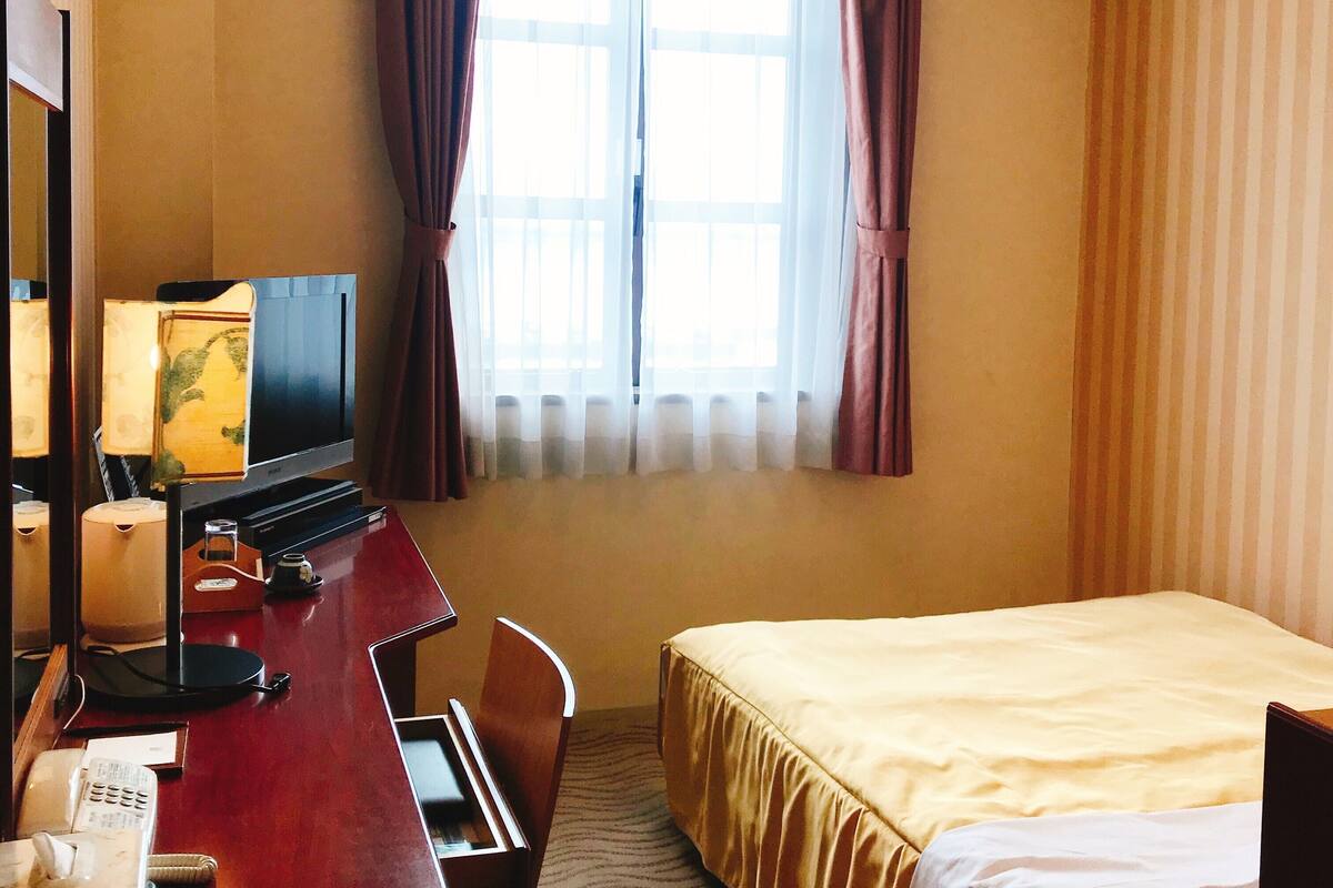 A hotel room with a bed, a desk with a television, a telephone, and a lamp.