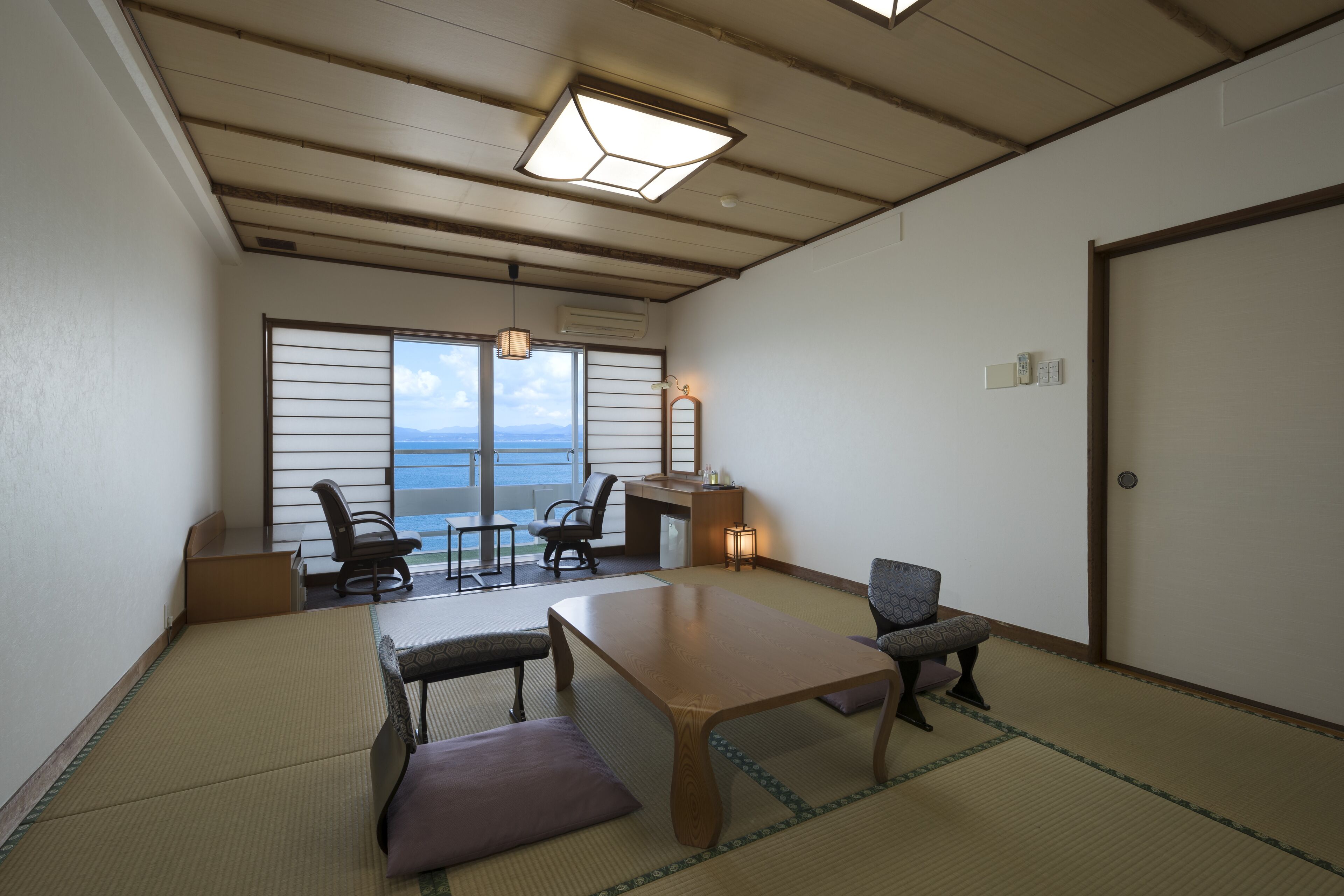 Una habitación japonesa tradicional con suelo de tatami, una mesa baja, sillas y vistas al mar.