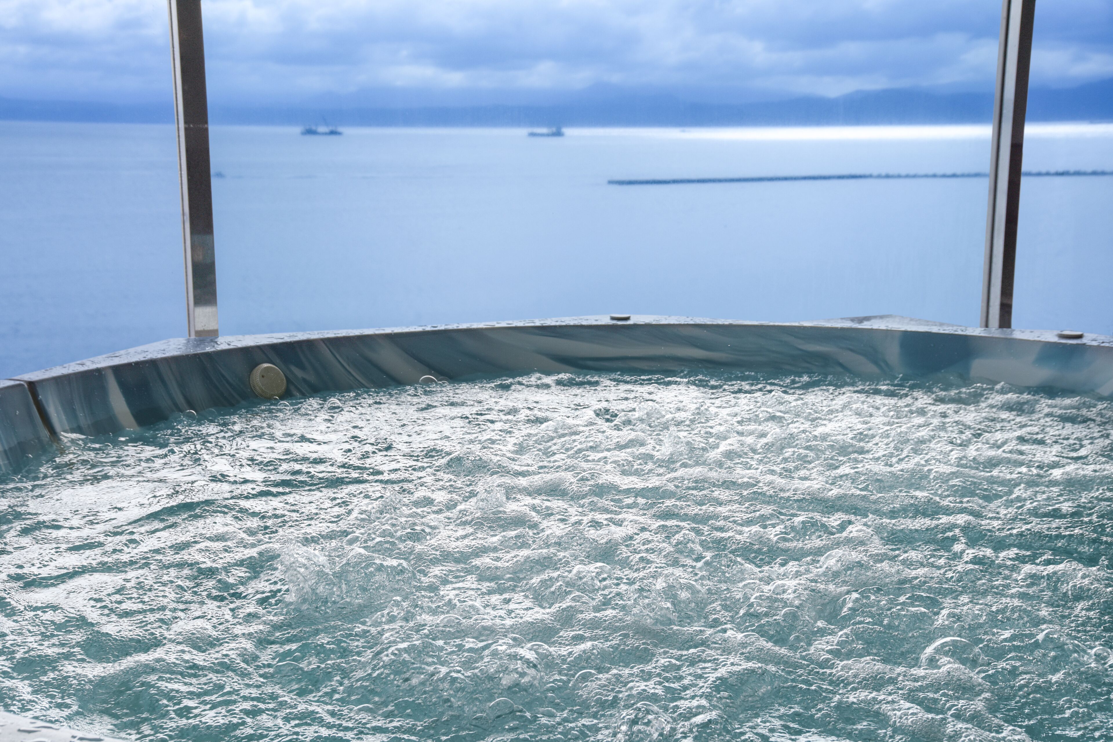 A hot tub with a view of the sea and distant ships.