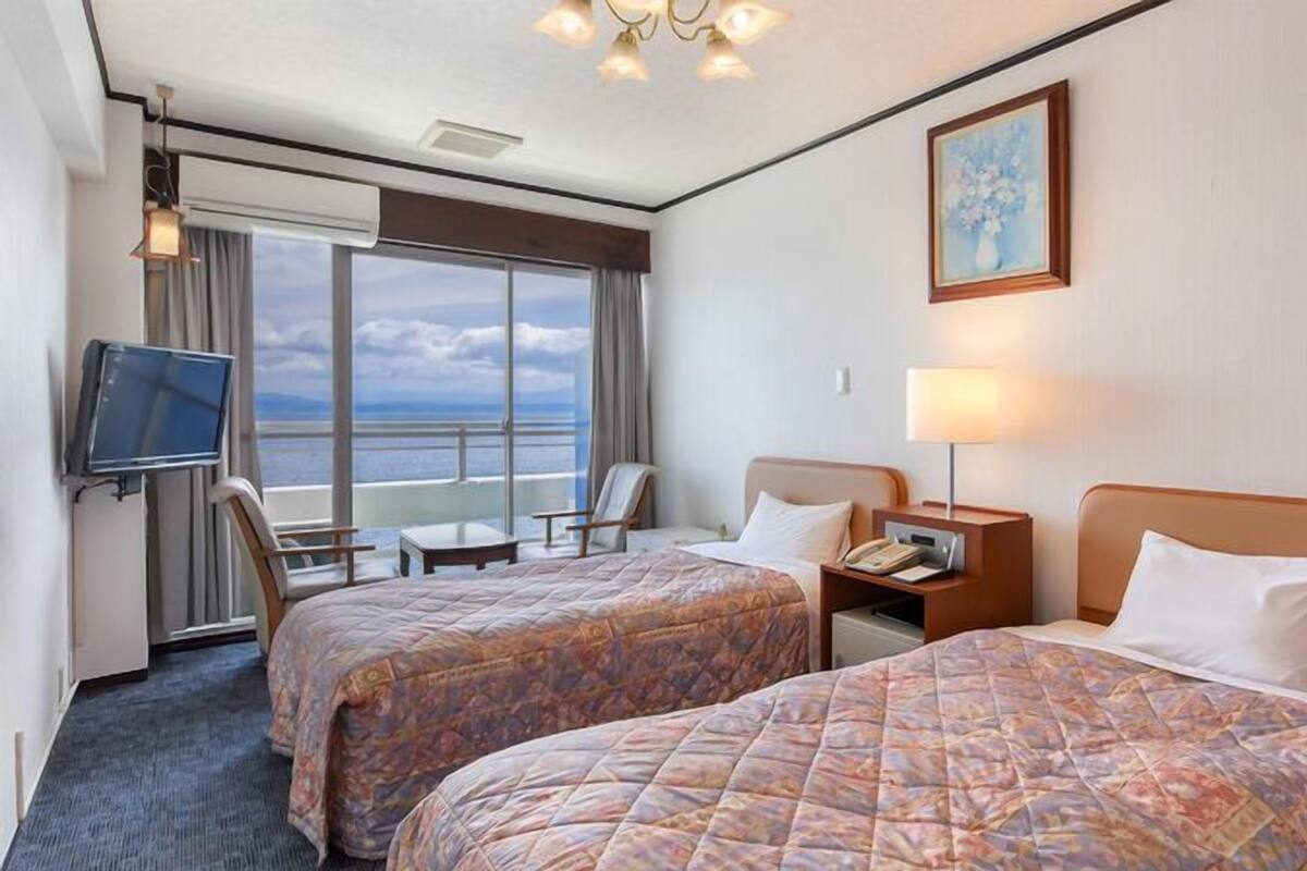 Habitación de hotel con dos camas, televisión, escritorio y vista al mar.