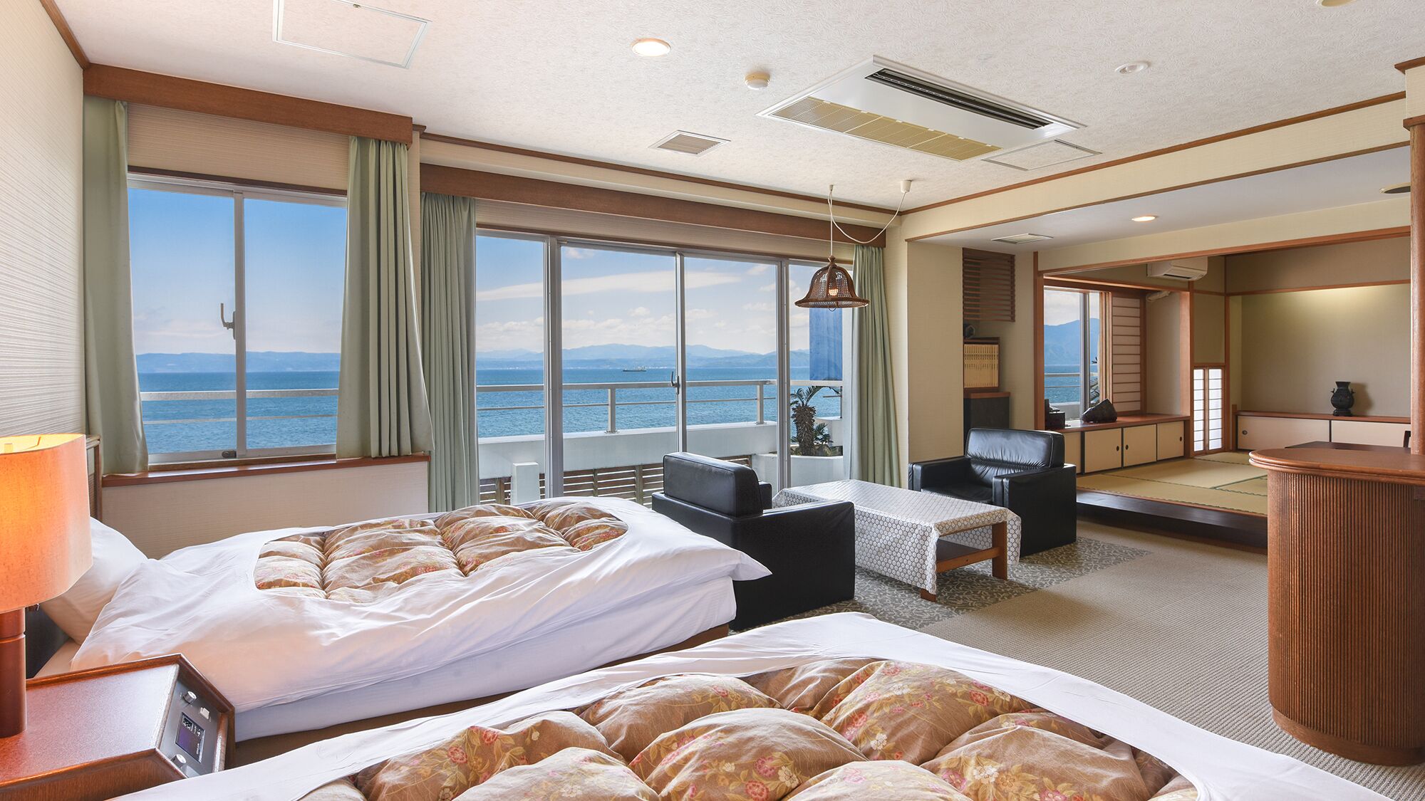 Habitación de hotel con dos camas, un escritorio, una silla, vista al mar y un balcón.