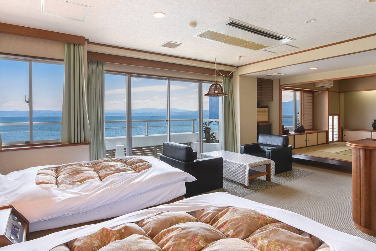 Habitación de hotel con dos camas, un escritorio, una silla, vista al mar y un balcón.