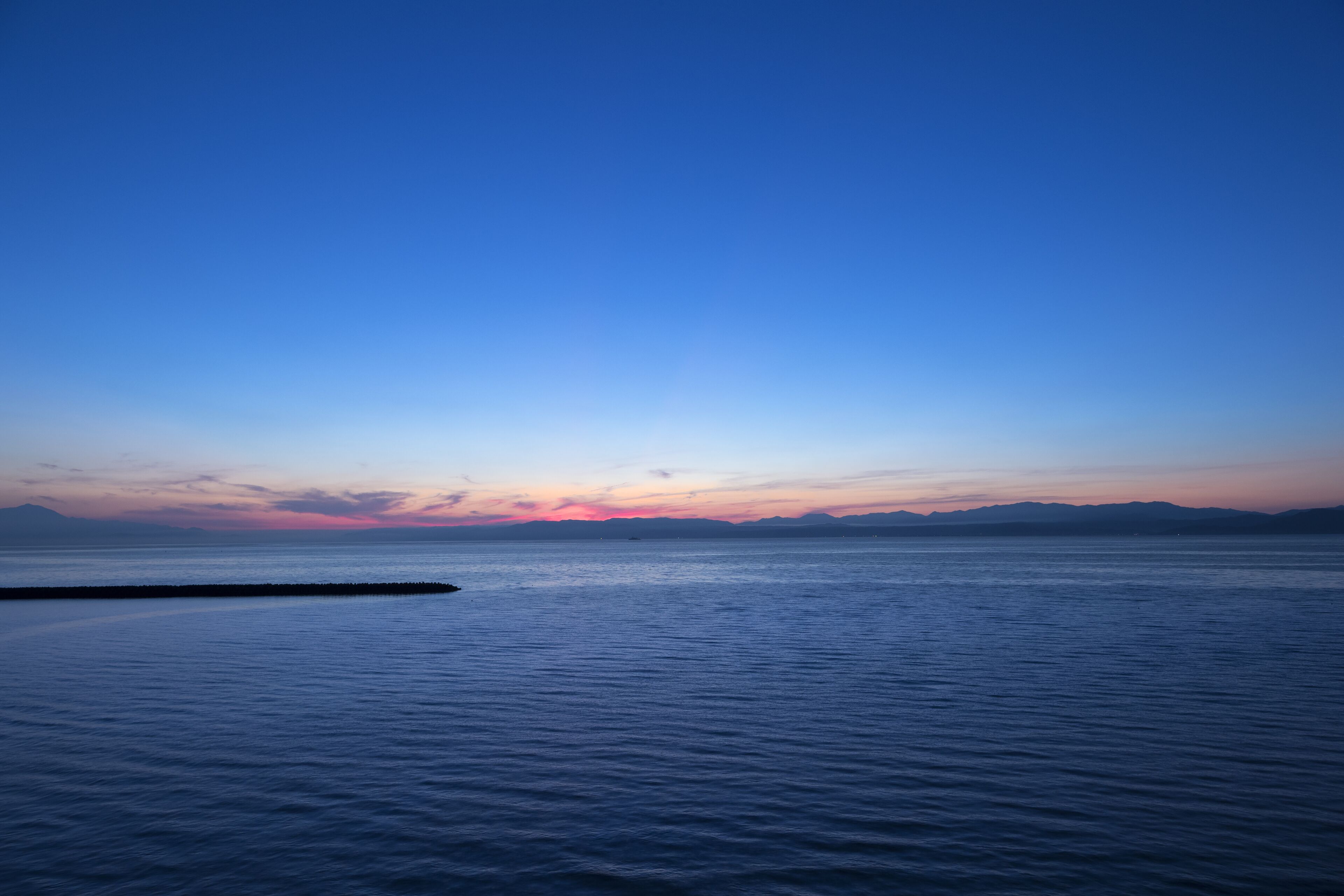 A calm sea at sunset with a clear sky.