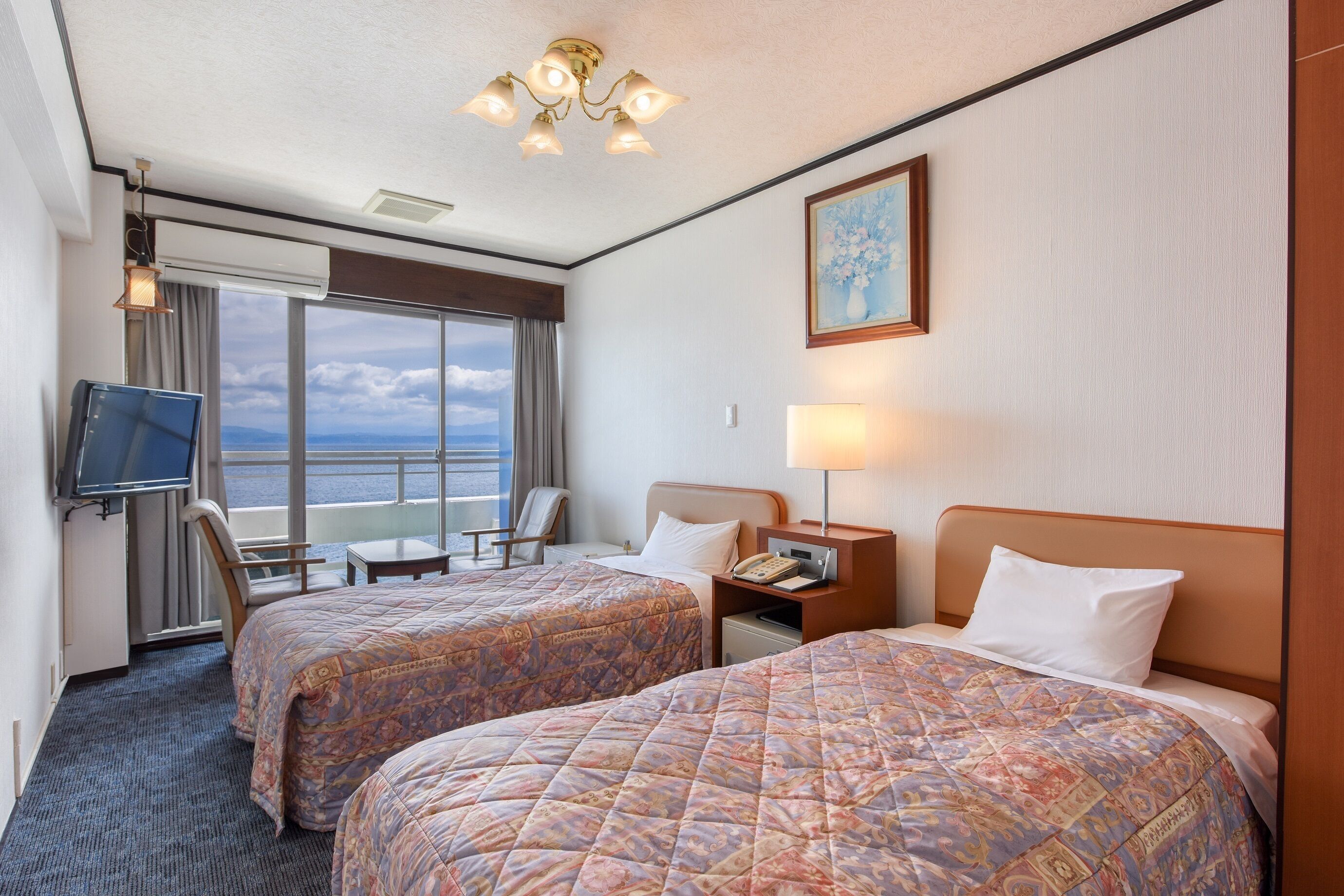 A hotel room with two beds, a TV, a desk, a chair, a window with a view, and a painting on the wall.