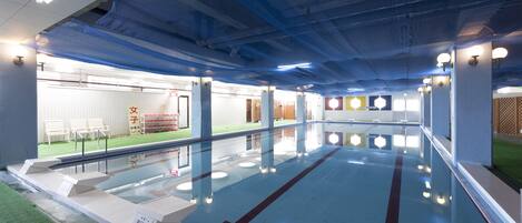 Una piscina interior con carriles claramente delimitados, una barrera de cristal y vistas al exterior con sillas y un cartel.