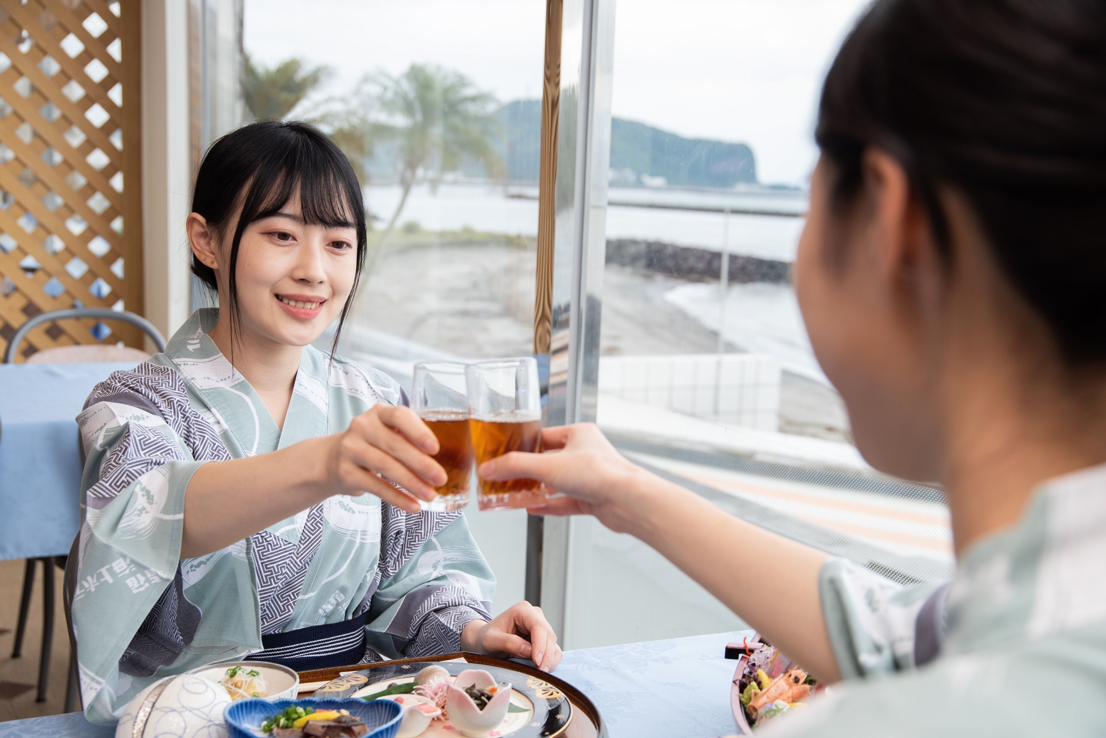 A person holding a glass of beer at a table with a view of a waterfront and a building in the background.