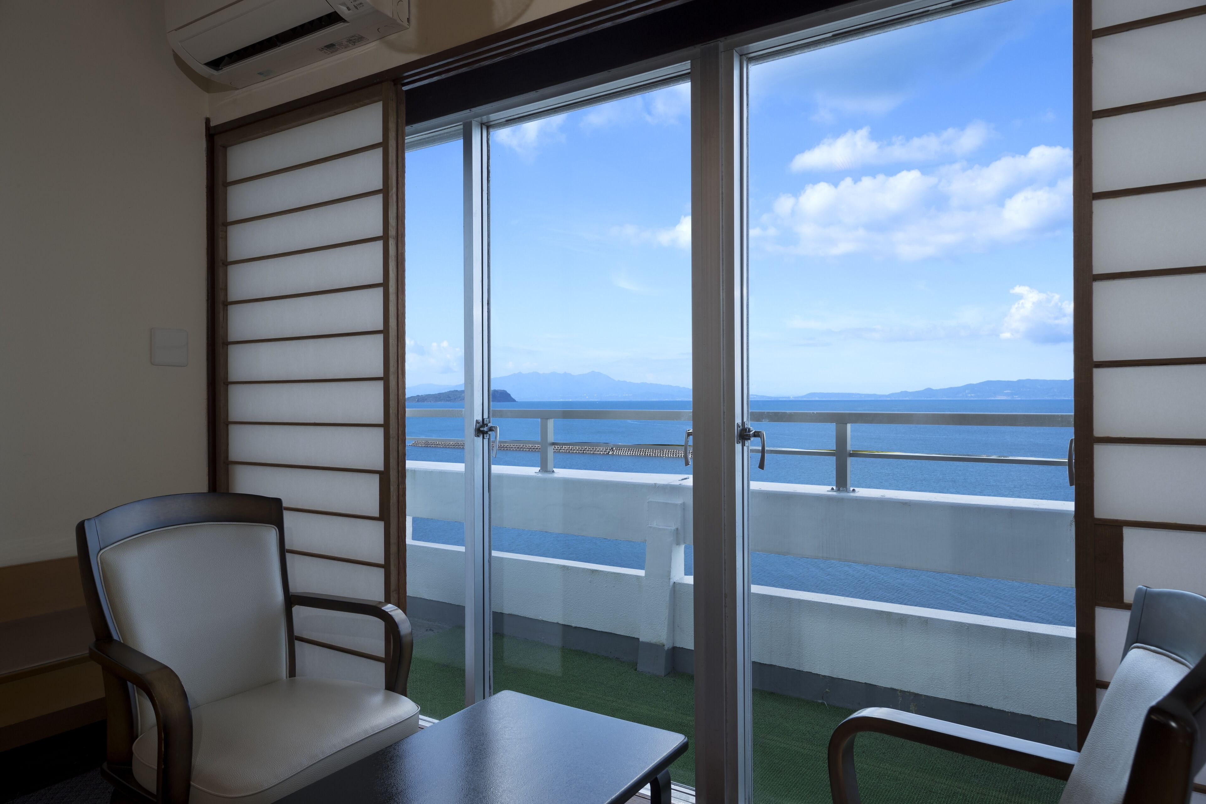 Balcón con vista al mar y a las montañas, con dos sillas y una mesa.