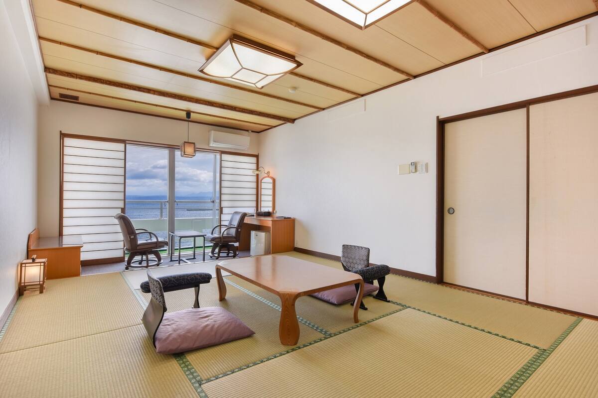 Una habitación japonesa tradicional con suelo de tatami, una mesa de madera baja y vistas al mar a través de paneles shoji.
