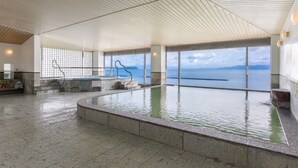 Una amplia piscina interior con vistas al mar, techo de madera y suelo de piedra.