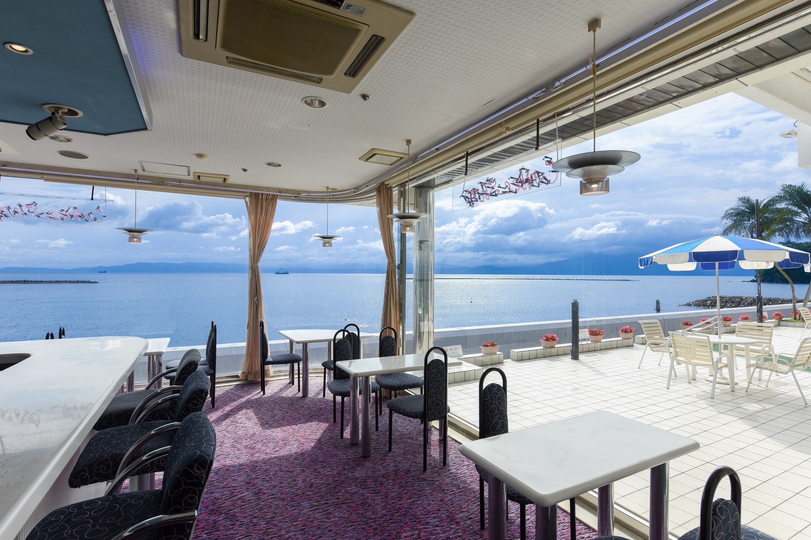 A restaurant with tables and chairs, a bar, and a view of the sea.