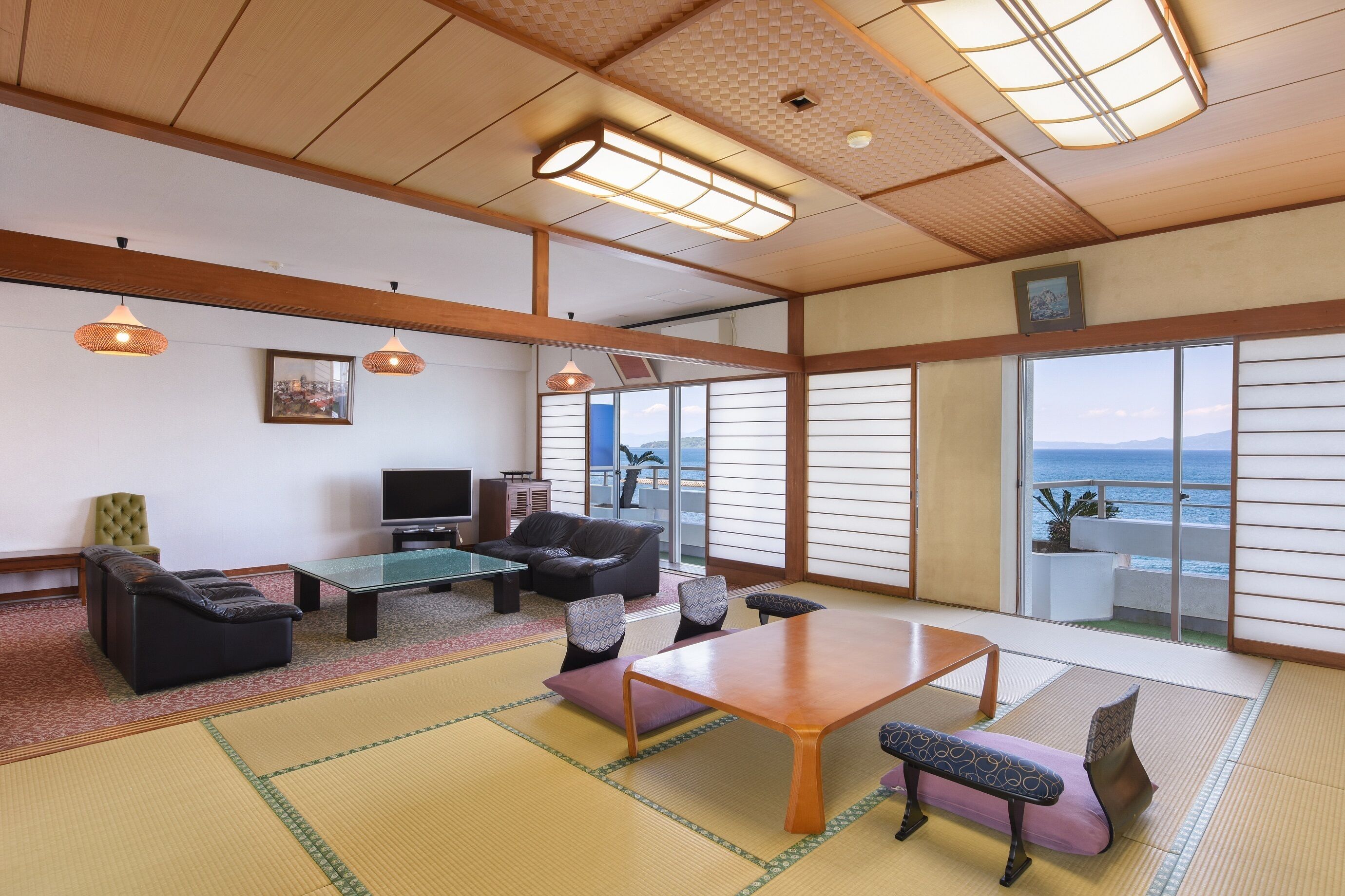 A traditional Japanese room with tatami flooring, a low table, sofas, and a television.