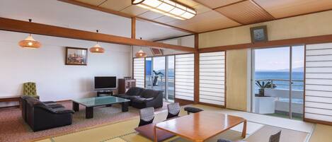 A traditional Japanese room with tatami flooring, a low table, sofas, and a television.