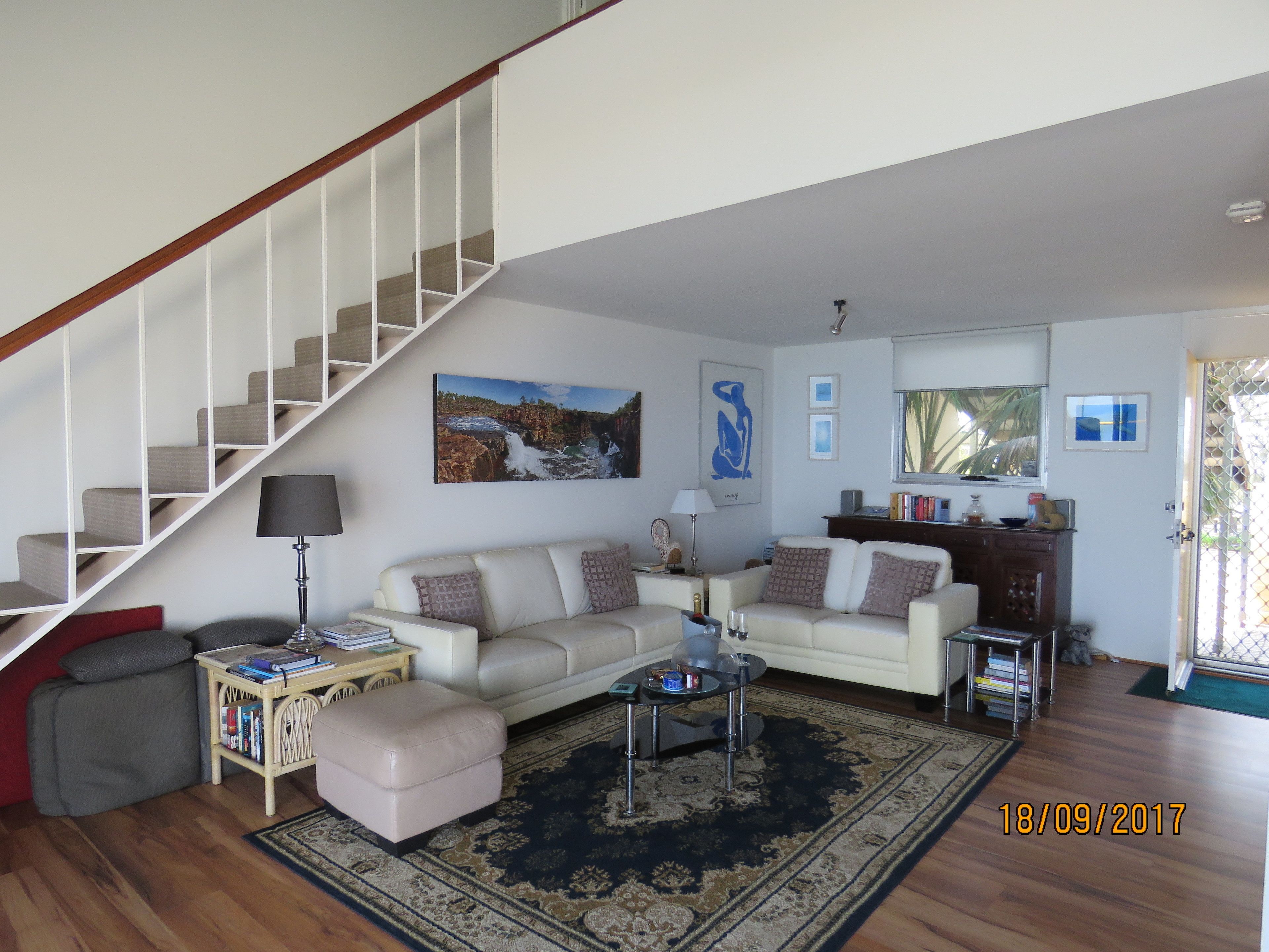 A spacious living room with a staircase, a sofa set, a coffee table, and a bookshelf.