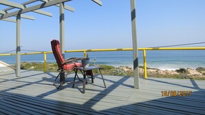 Une terrasse avec une chaise rouge et une table, d’où l’on a une vue sur l’océan.