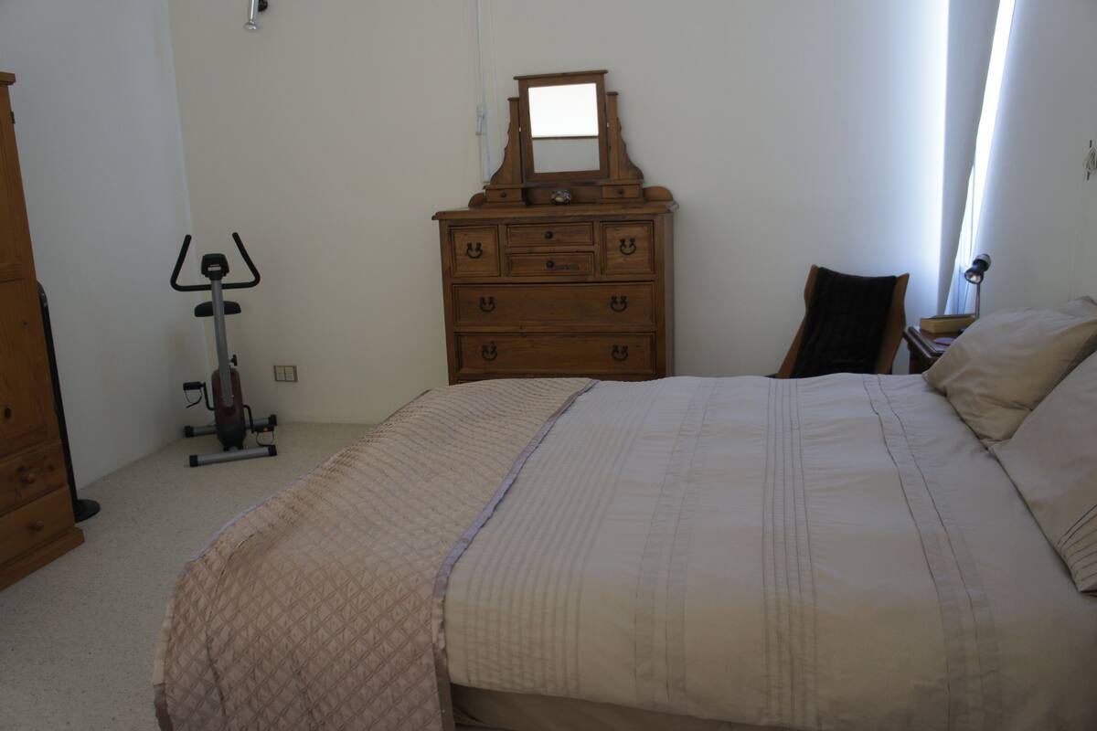 A bedroom with a bed, a dresser, a mirror, and a stationary exercise bike.