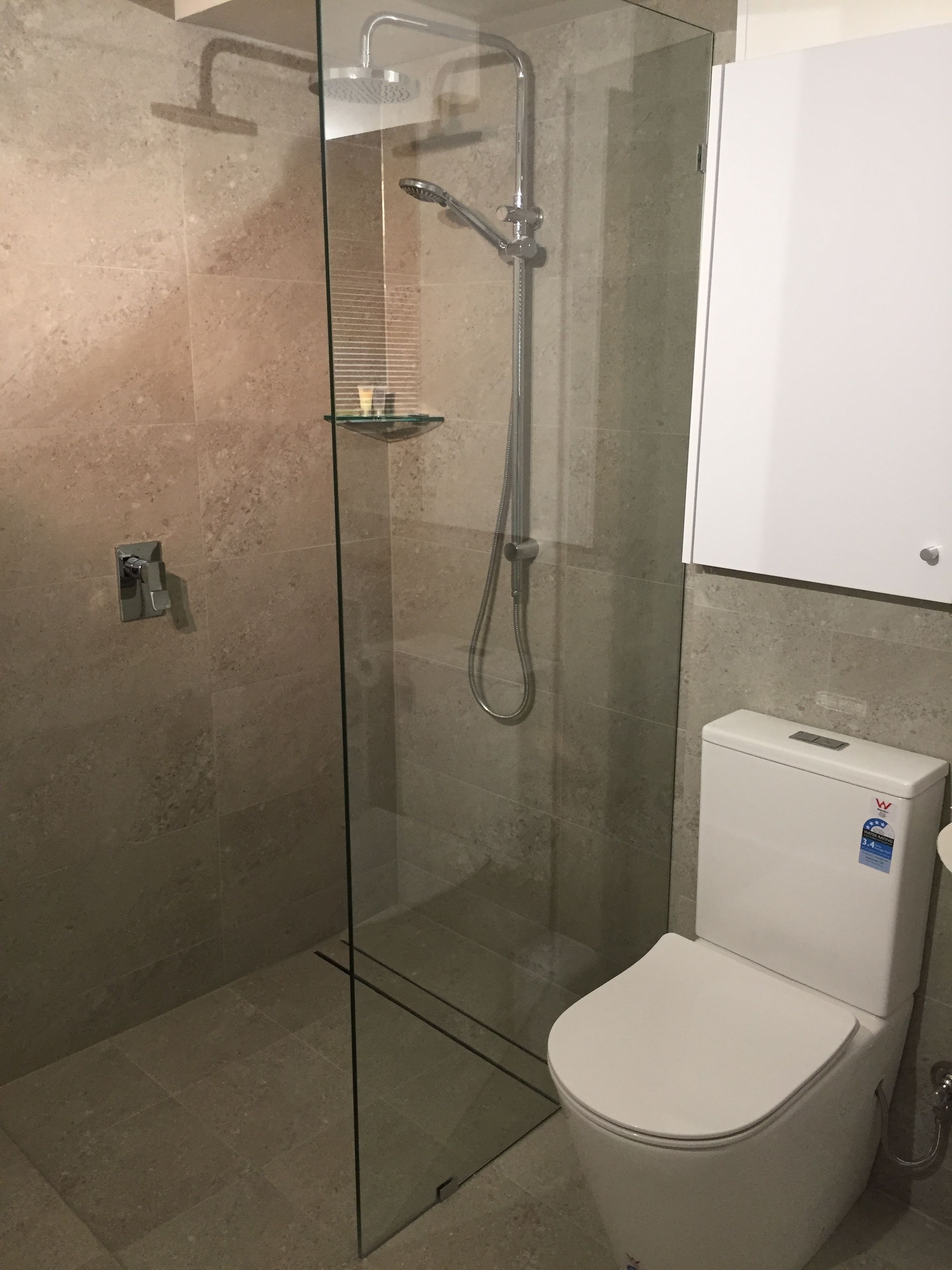A modern bathroom with a glass-enclosed shower, a white toilet, and a glass shelf.