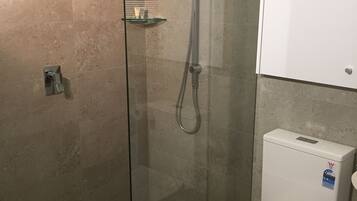 A modern bathroom with a glass-enclosed shower, a white toilet, and a glass shelf.