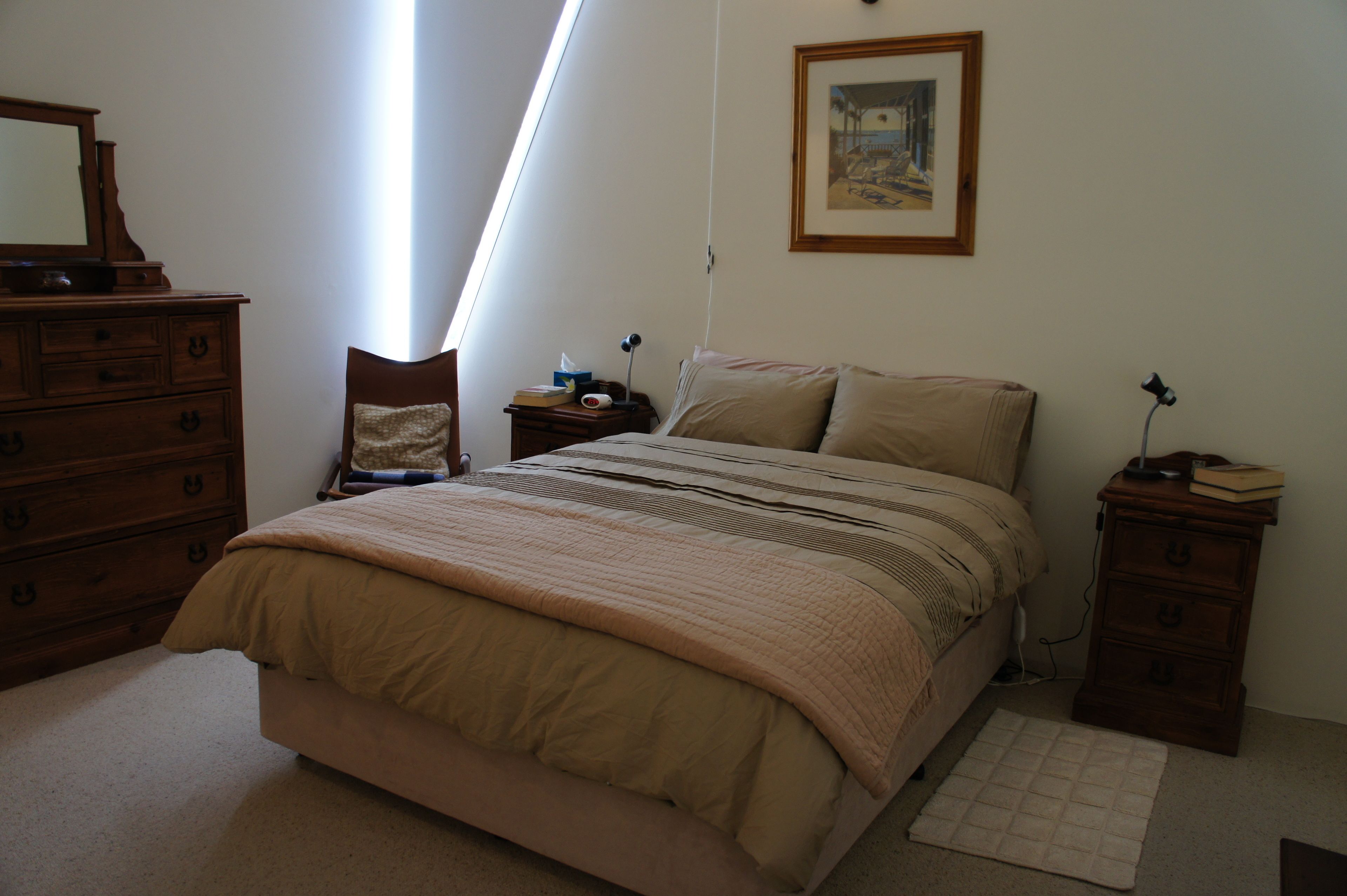 A bedroom with a bed, dresser, chair, bedside table, lamp, and a framed picture on the wall.