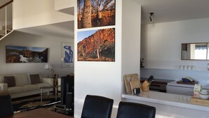 Un salon moderne avec un canapé, une table basse et des œuvres d’art. On aperçoit également un coin repas avec une table et des chaises.