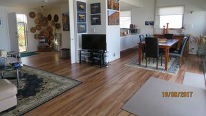 Un vaste espace de vie doté d’un plancher en bois, d’un téléviseur à écran plat, d’une table à manger avec des chaises et d’un coin cuisine équipé d’un four à micro-ondes.