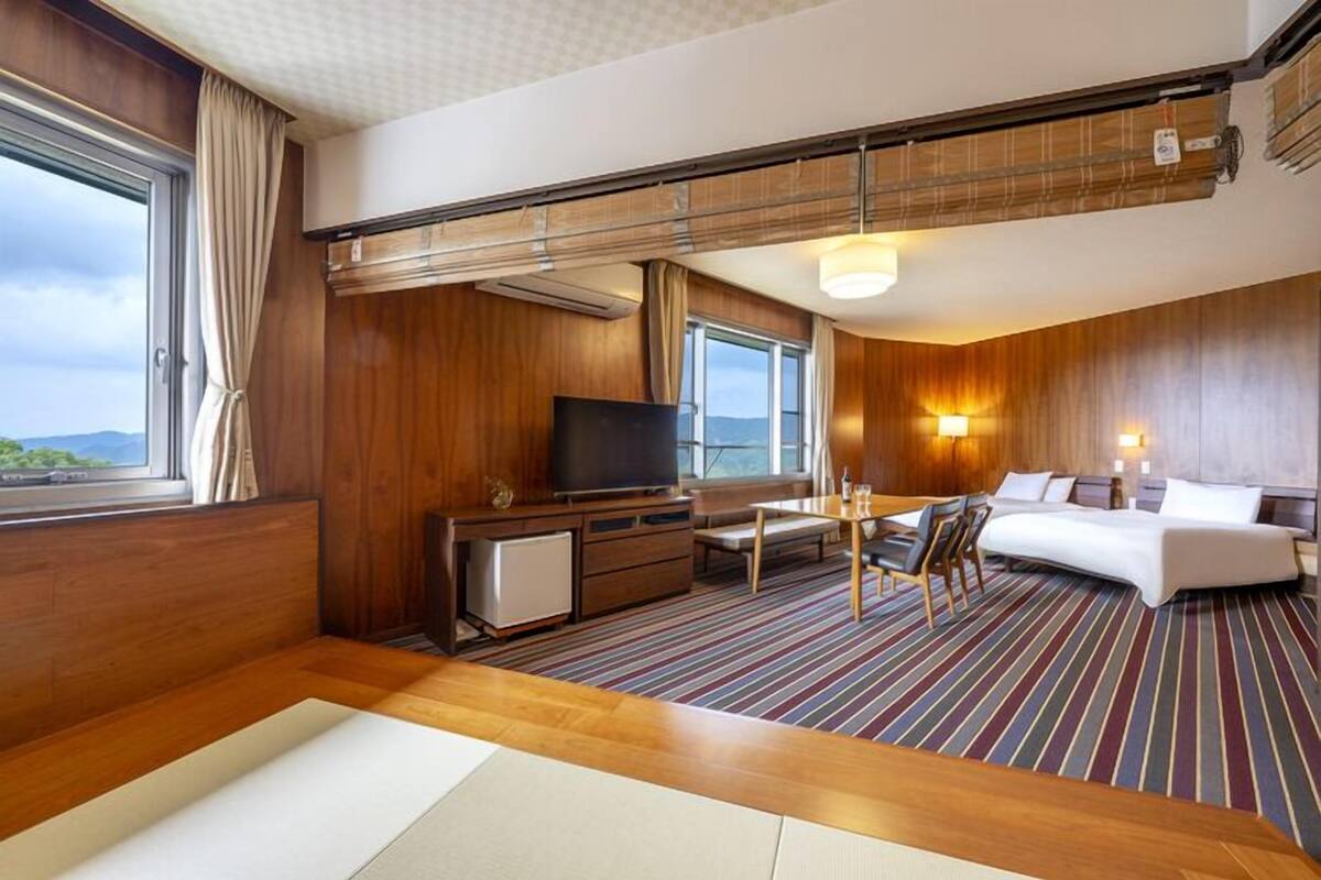 Habitación de hotel con piso de madera, una cama, televisor, escritorio y ventana con vista.