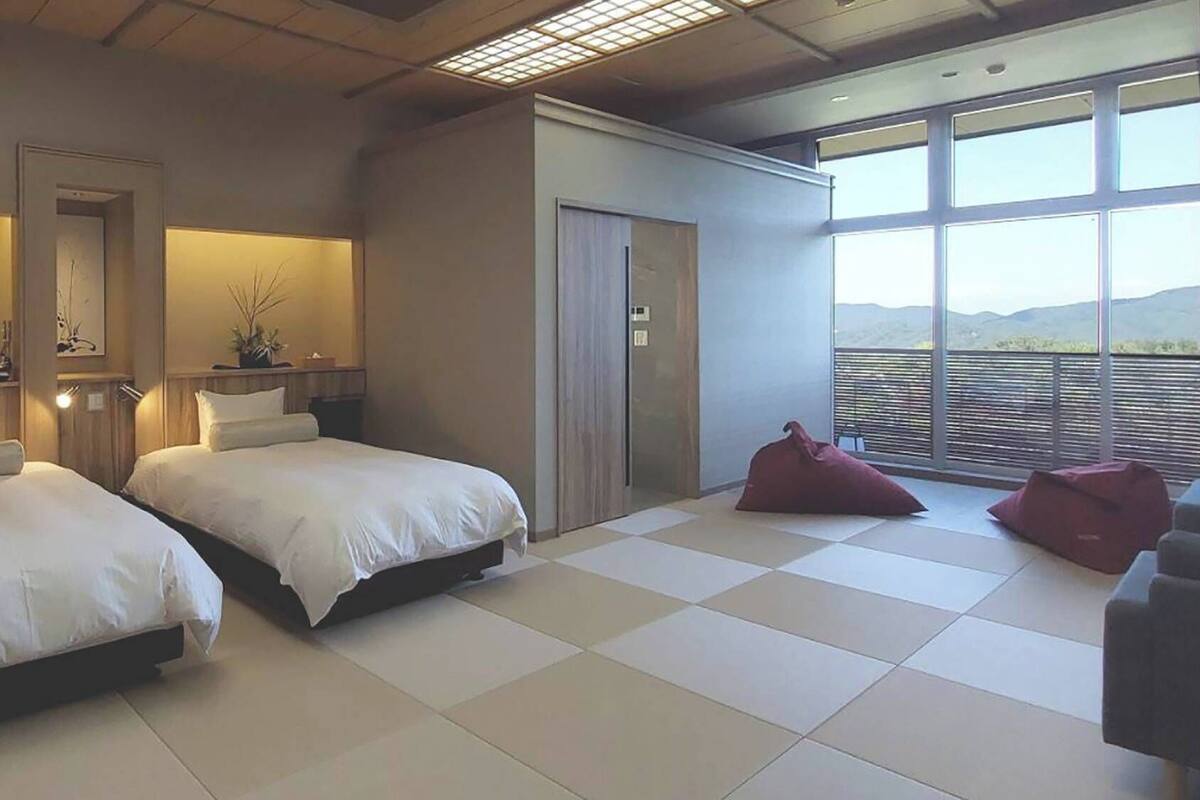 Habitación de hotel con dos camas, un ventanal con vistas y un balcón.