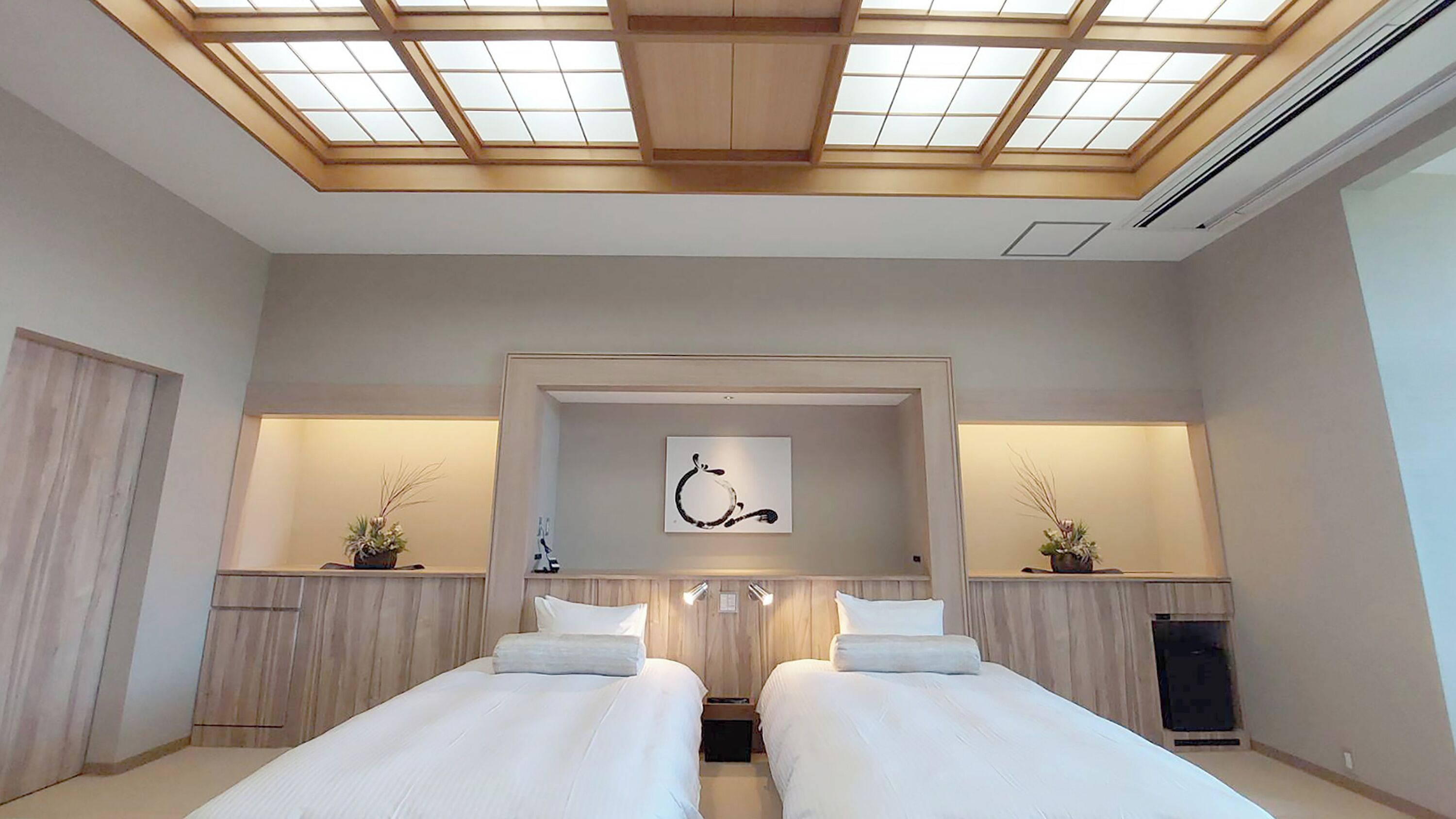 A hotel room with two beds, a skylight, a painting, and a small plant on the nightstands.