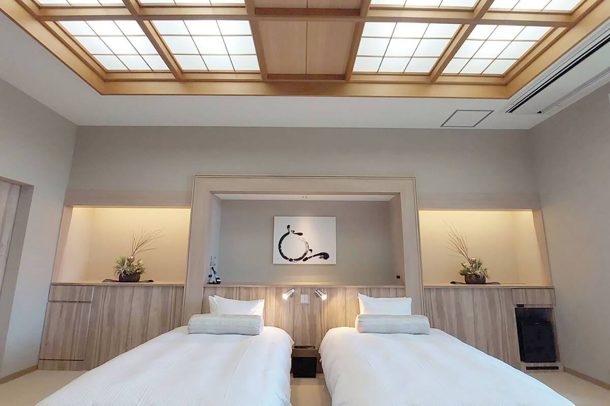 Habitación de hotel con dos camas, un tragaluz, un cuadro y una planta pequeña en las mesitas de noche.