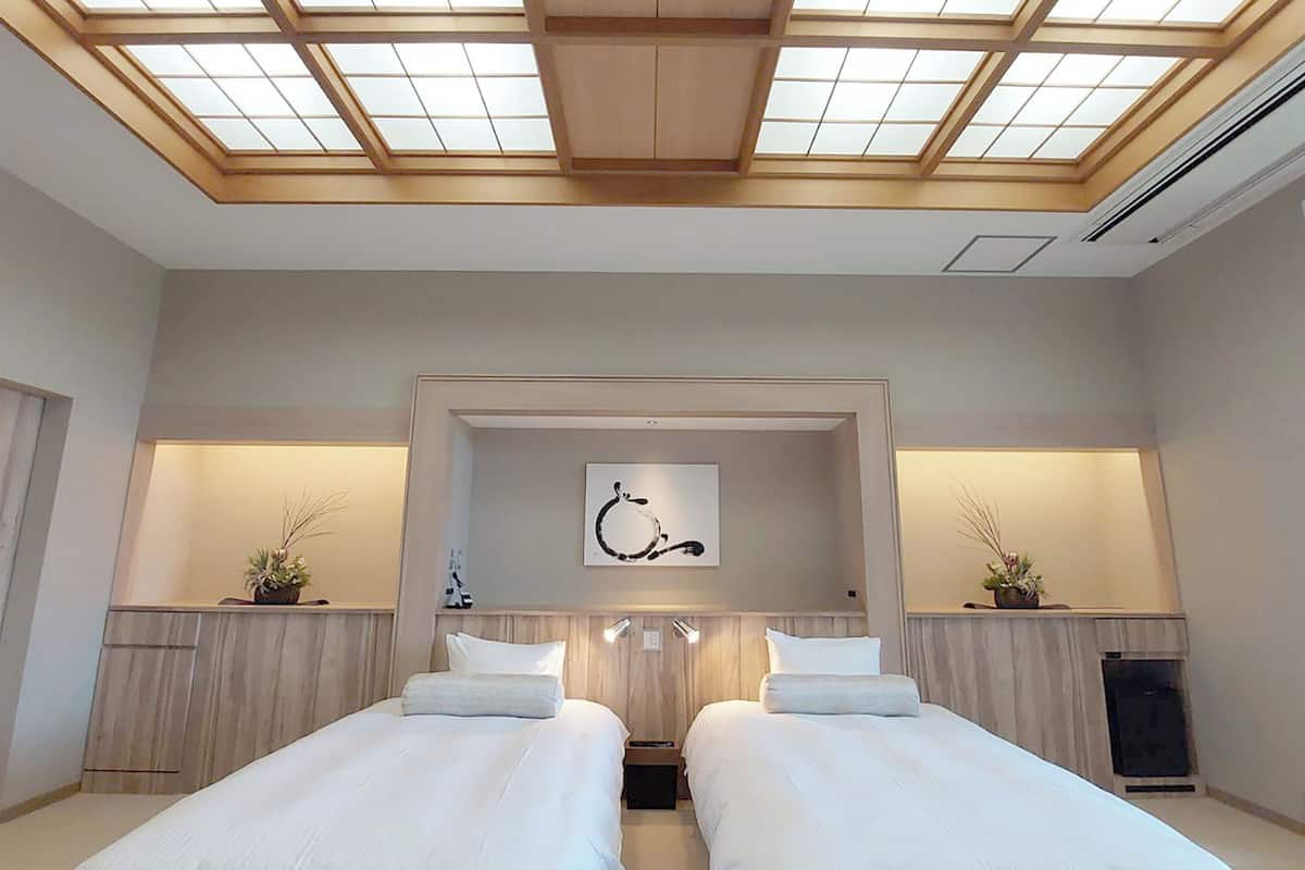 A hotel room with two beds, a skylight, a painting, and a small plant on the nightstands.