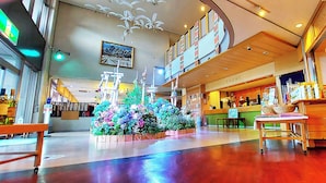 A spacious atrium with a central floral arrangement, a reception desk, and a high ceiling with decorative lighting. - Ikoinomura Heritage Minoyama (Minano)