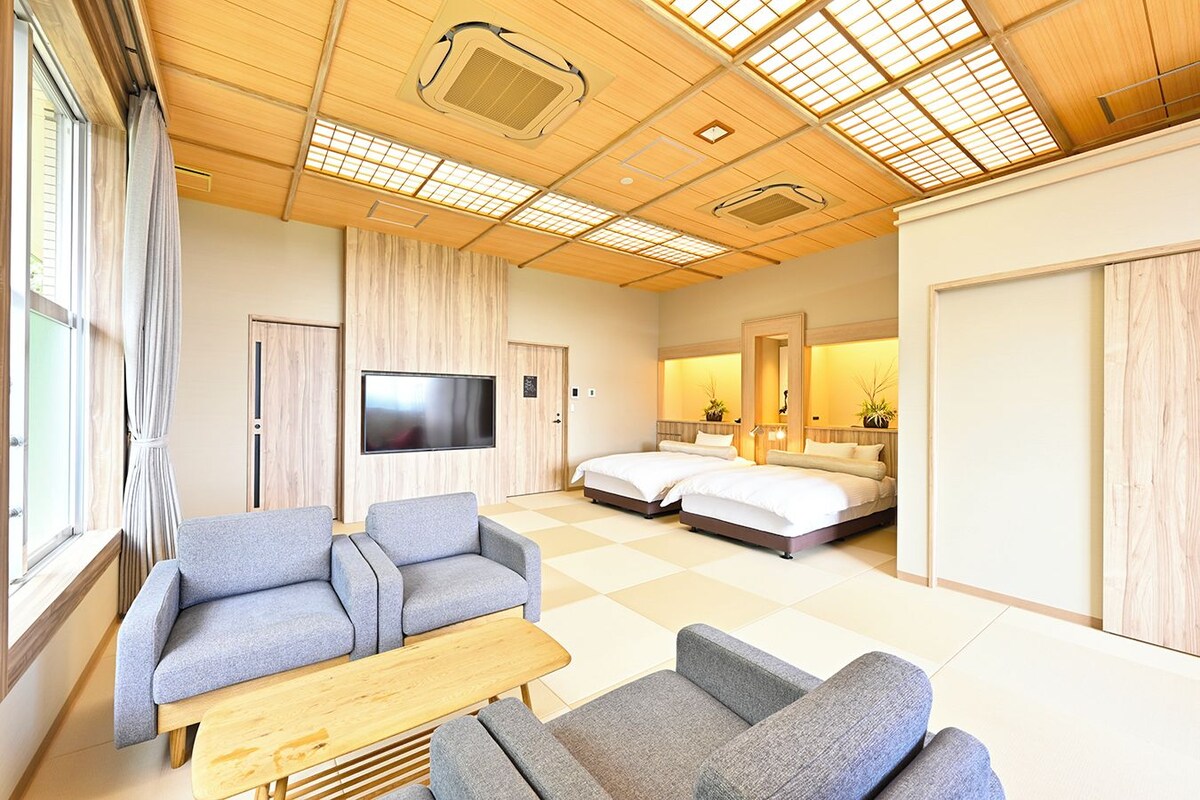 A hotel room with a sofa, a bed, a TV, and a wooden ceiling with skylights.