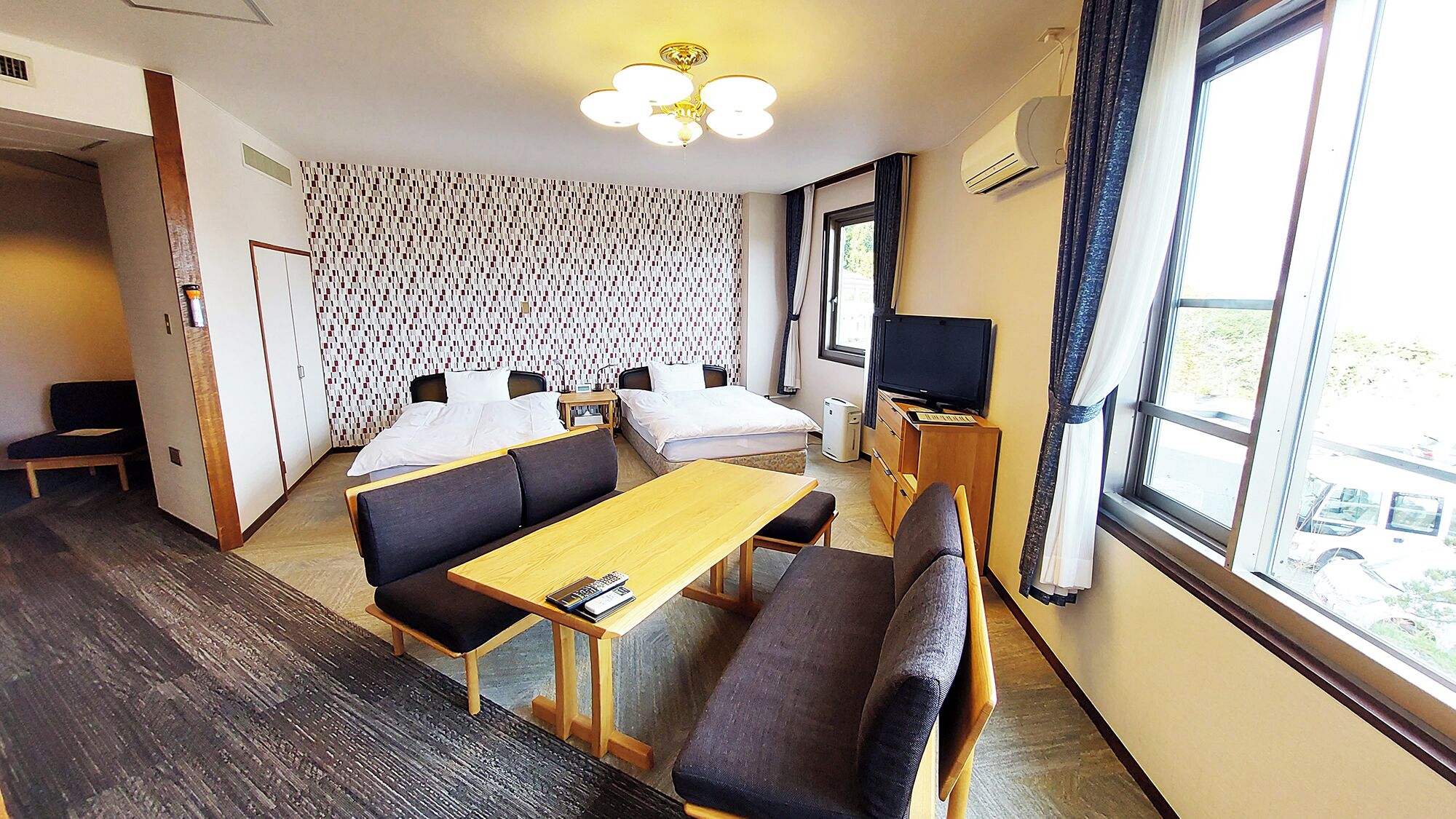 A hotel room with a bed, sofa, table, TV, and a patterned wall.