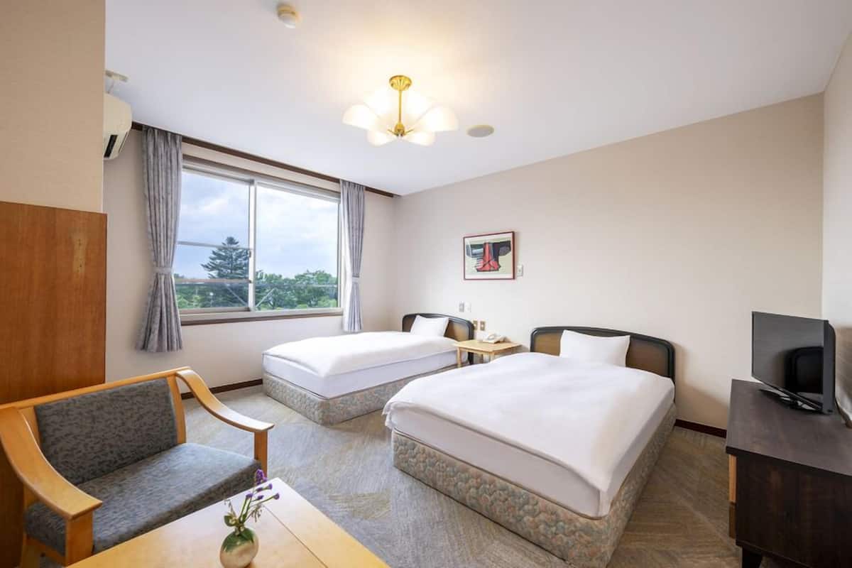 A hotel room with two beds, a desk, a chair, a television, and a window with curtains.