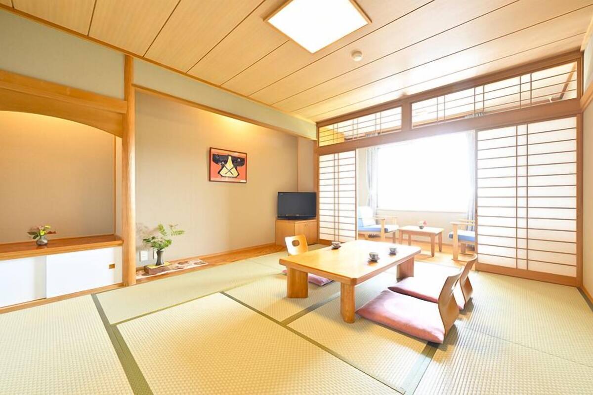 Una habitación japonesa tradicional con suelo de tatami, una mesa baja, un televisor y puertas correderas.