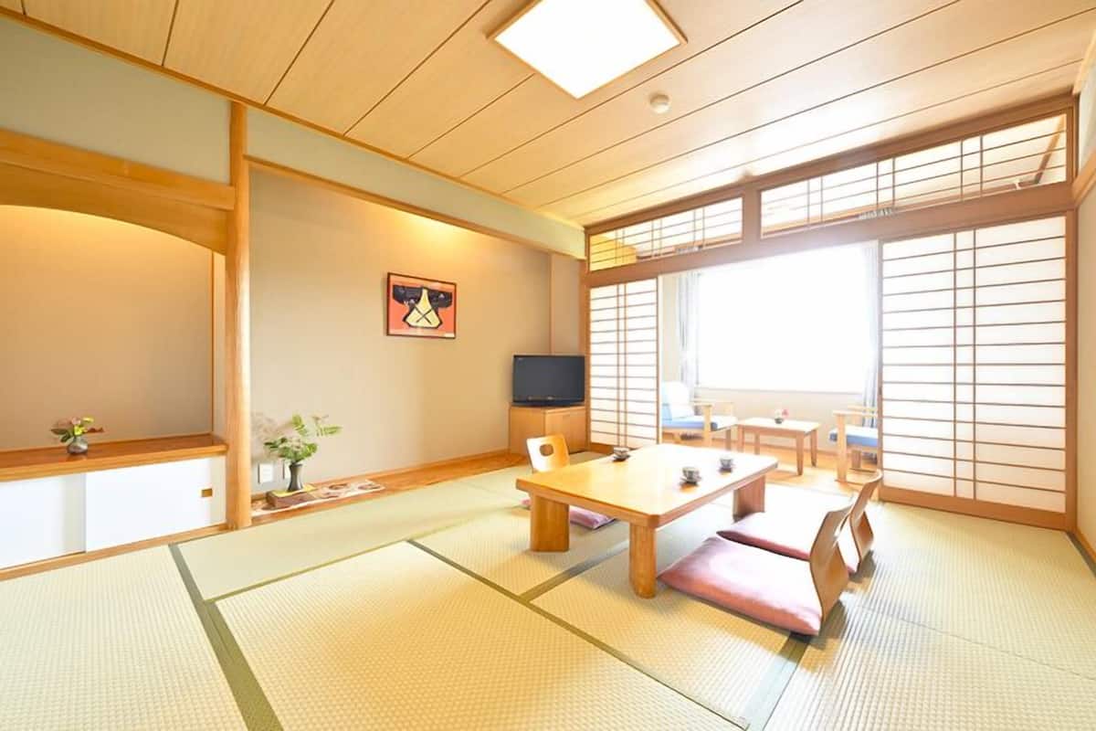 A traditional Japanese room with tatami flooring, a low table, a television, and sliding doors.