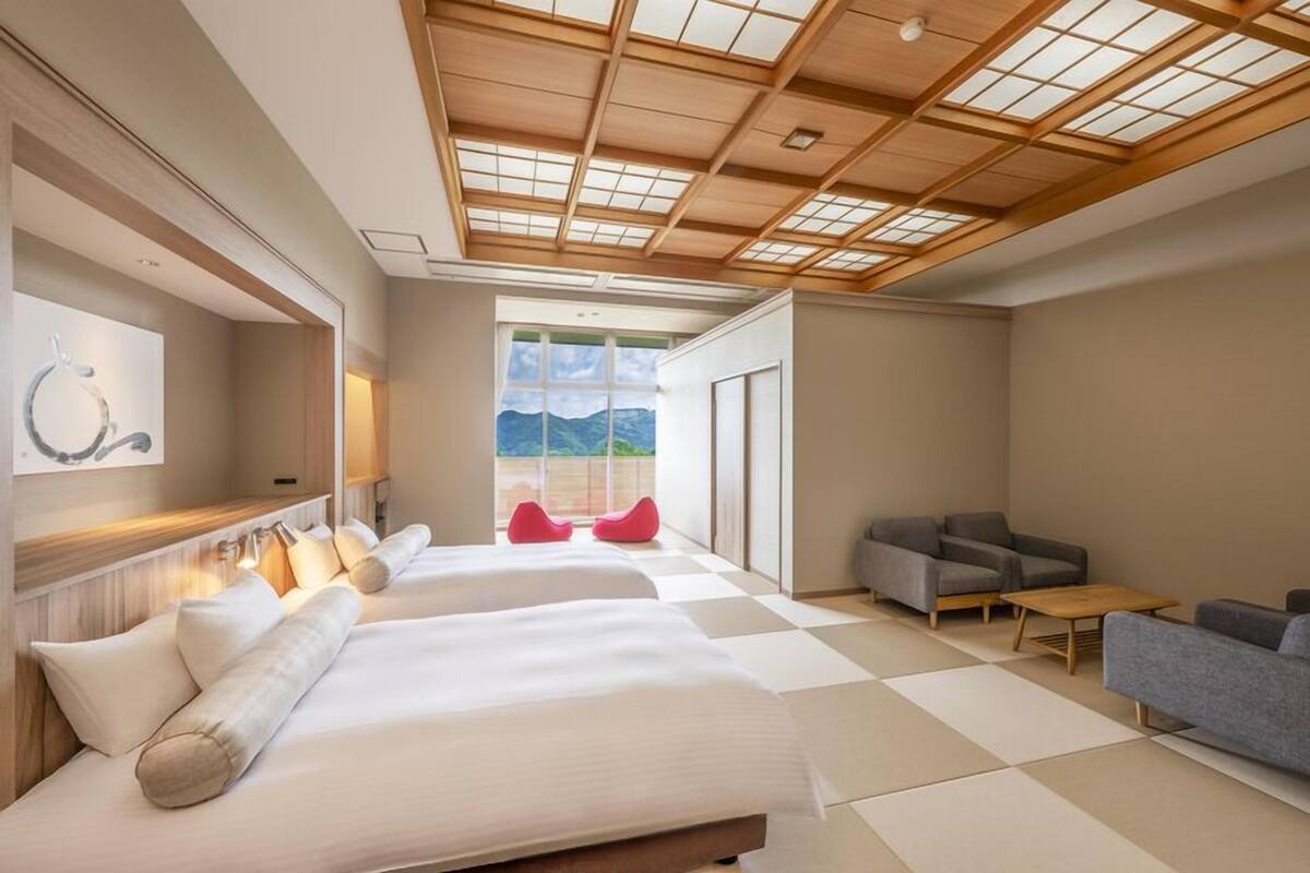 Una habitación de hotel moderna con una cama grande, un sofá, una mesita y vistas al exterior.