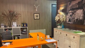 Hotelkamer met een houten wand, een ingelijst kunstwerk, een bureau met een computer, een stoel en een kast met een bloemenvaas.