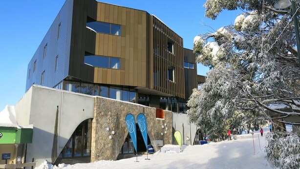 Een modern gebouw met een stenen gevel en grote ramen, omringd door met sneeuw bedekte bomen.