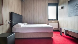 Hotelkamer met een bed, nachtkastje, bankje, een aan de muur bevestigde televisie en een raam.